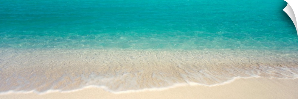 Panoramic photograph displays the clear waters of the Atlantic Ocean gently crashing into the sandy beach of an island.