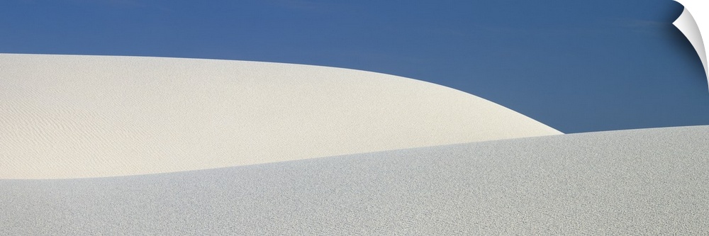 Panoramic photograph of the sloping dunes of White Sands, New Mexico, contrasting with the darker sky, creating a minimali...