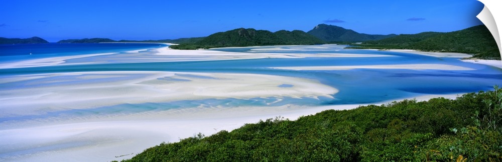 Panoramic view of white beaches and water surrounded by hills and dense forest.