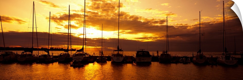 Panoramic photograph of many boats in a line, docked in Egg Harbor beneath a vibrant setting sun, in Door County, Wisconsin.
