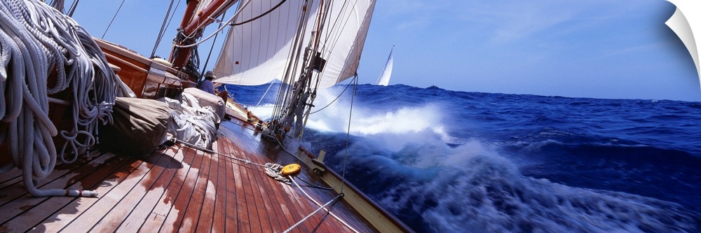 The deck of a yacht covered with ropes and raised sails tossing in the waves of this panoramic photograph.