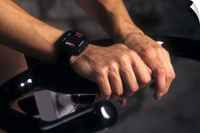 Detail of hands on stationary bike with heart rate monitor watch