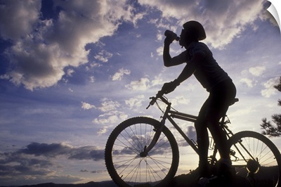 Silhouette of mountain biker drinking at the summit during sunset