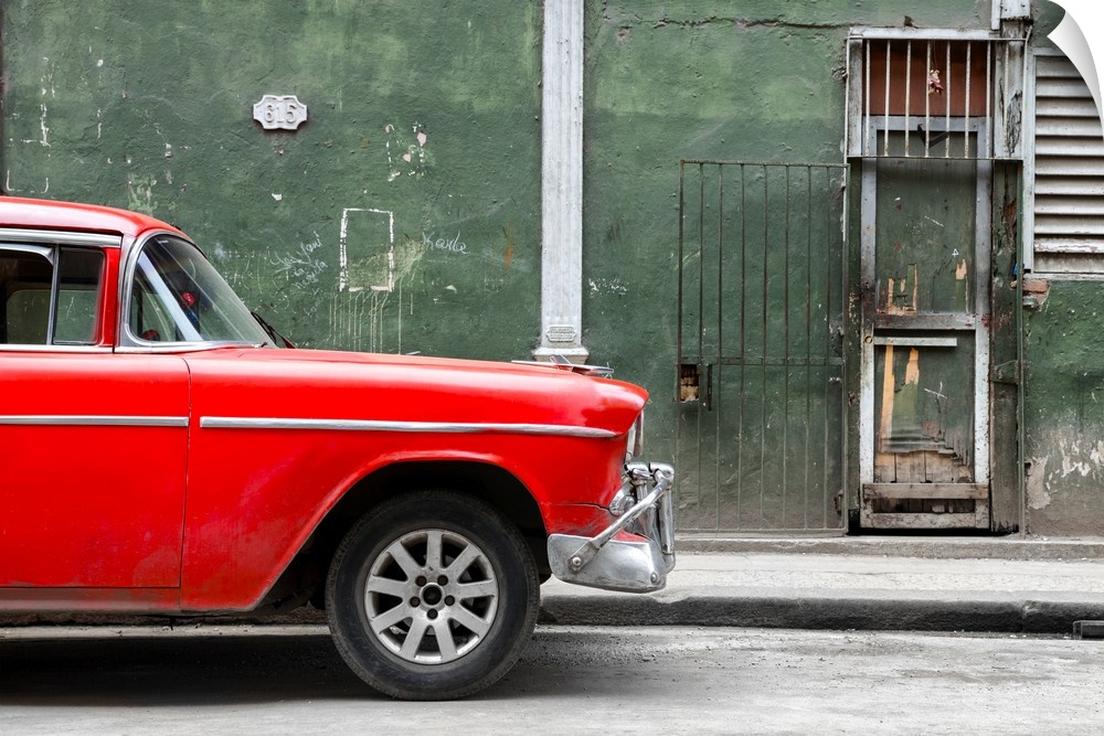 Photograph of the front of a bright red vintage car with a dark green building in the background creating contrast.