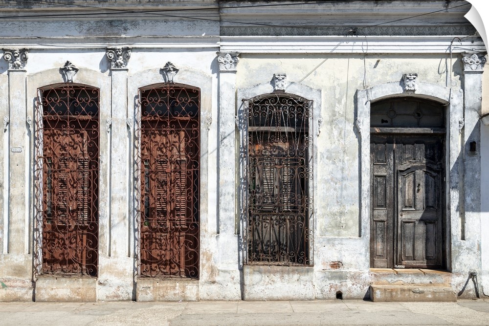 Photograph of an aged Cuban facade with windows and a wooden door.