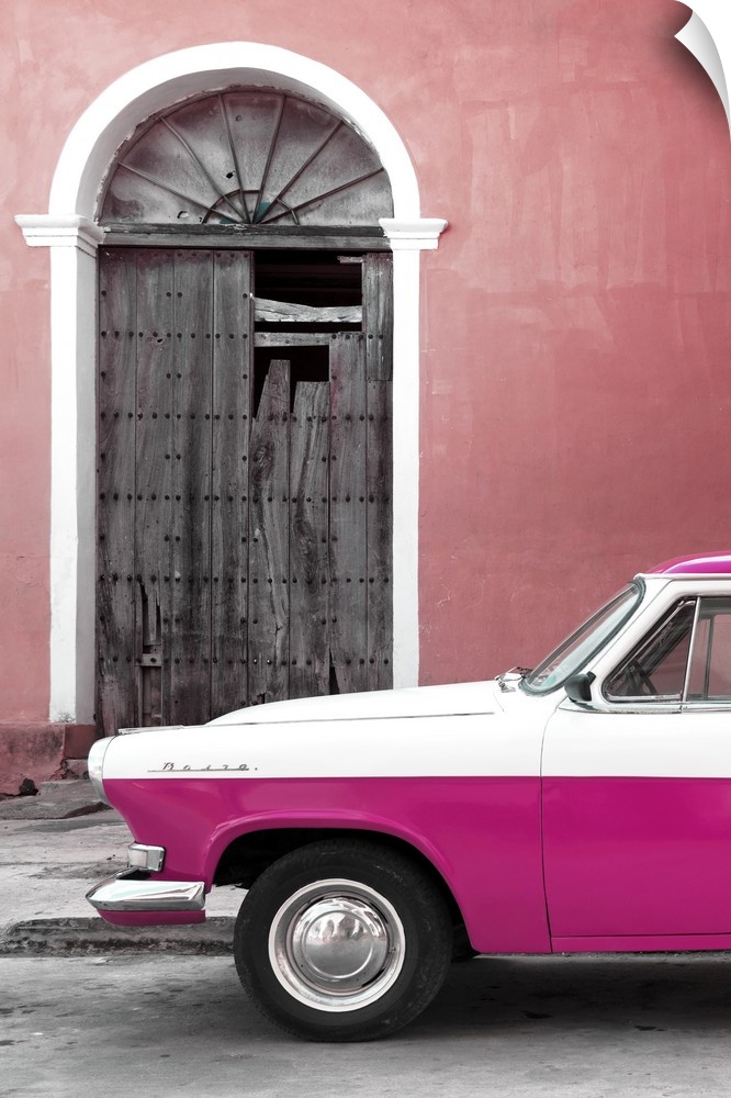 Photograph of the front of a vintage pink and white car outside of a pink building with a broken wooden door.