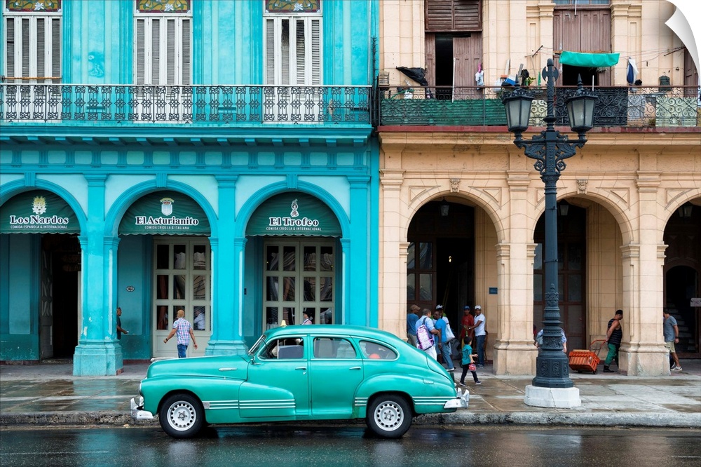 Photograph of a turquoise vintage car parked outside of a bright blue building in downtown Havana.
