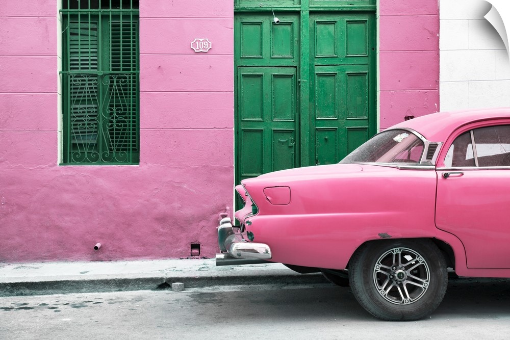 Photograph of the back of a pink vintage car next to a matching facade with a green wooden door and window.