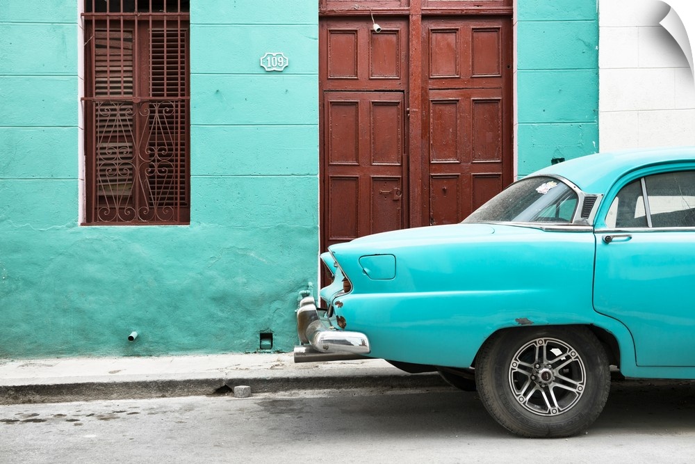 Photograph of the back of a turquoise vintage car next to a matching facade with a dark wooden door and window.