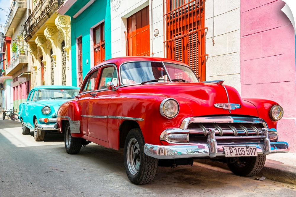 Photograph of a turquoise and a red vintage Chevrolets parked along a colorful Havana street scene.