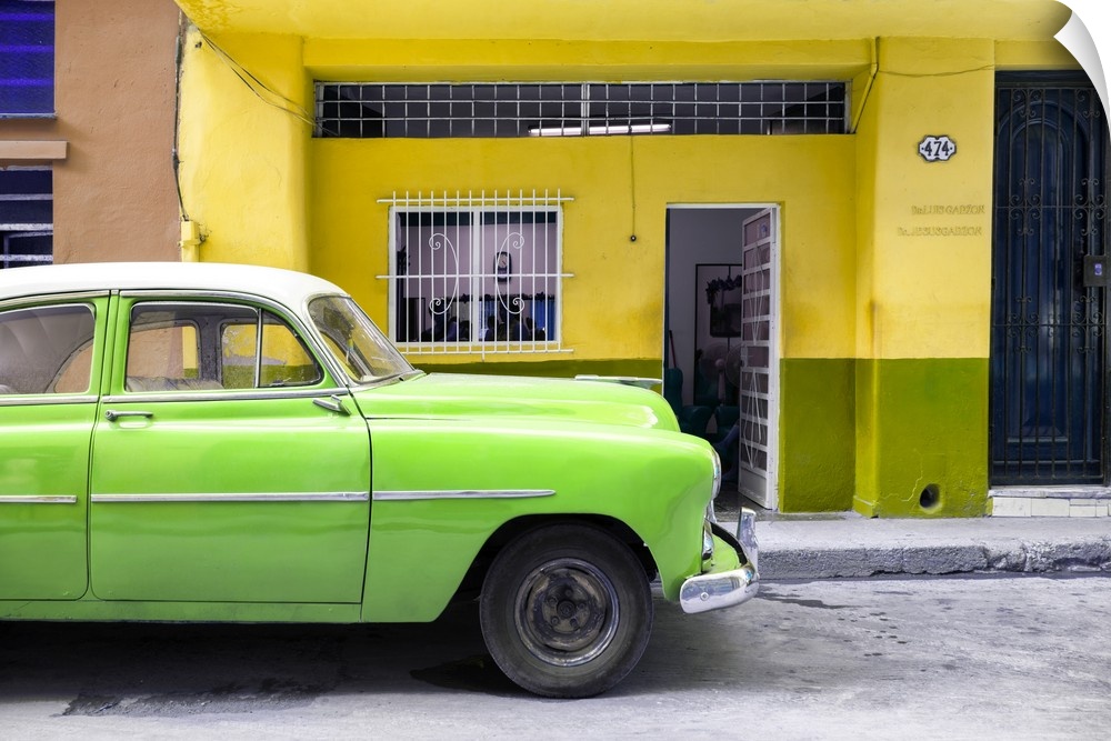 Photograph of a bright green vintage car parked on the road in Havana with a bright yellow facade in the background.
