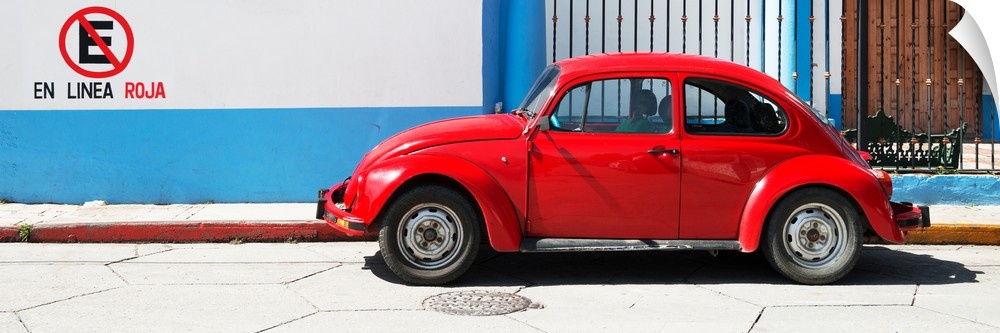 Panoramic photograph of a red Volkswagen Beetle parked in front of a building with blueand white walls. From the Viva Mexi...