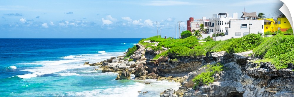 Panoramic photograph of the Isla Mujeres coastline displaying a rocky shore and buildings in the distance. From the Viva M...
