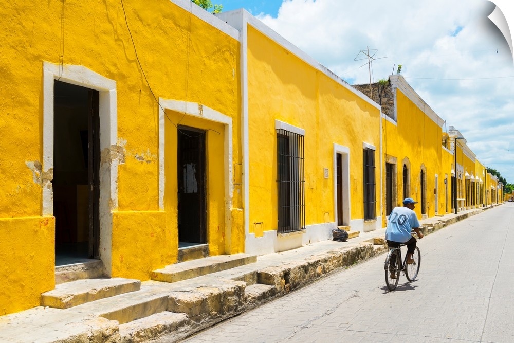 Pphotograph highlighting the yellow buildings in Izamal, Yucat?n, Mexico, with a man in blue riding a bicycle down the roa...
