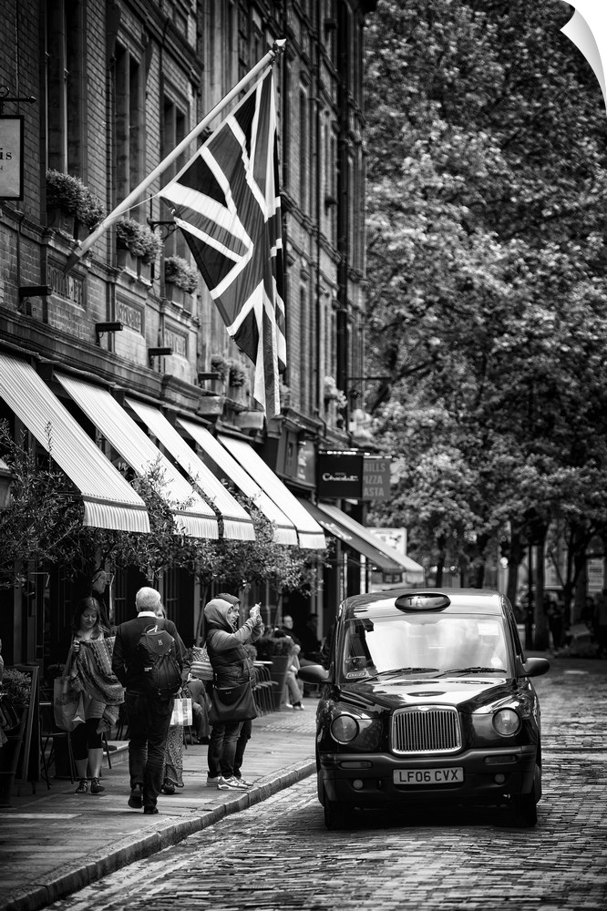 Black and white image of a taxi cab on the street next to awnings in London, England.