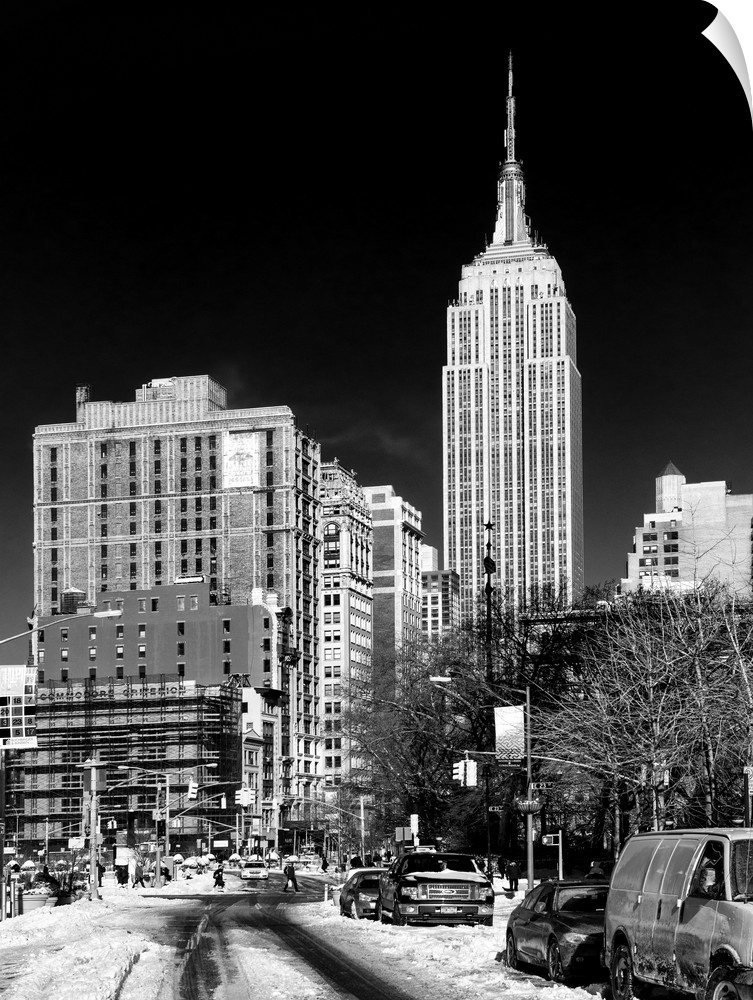 A black and white photograph of the Empire state building standing tall in NYC, seen from street level.
