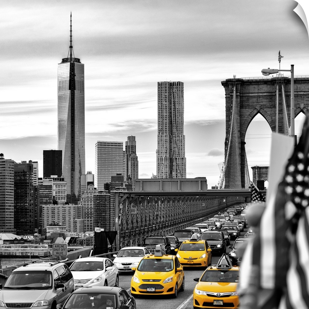A black and white photograph of the One World Trade building from the Brooklyn bridge with yellow taxis on the bridge.