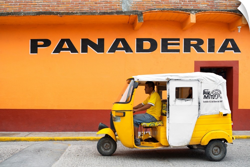 Photograph of a yellow Tuk Tuk (taxi) driving on the street in front of a bakery with orange exterior walls. From the Viva...