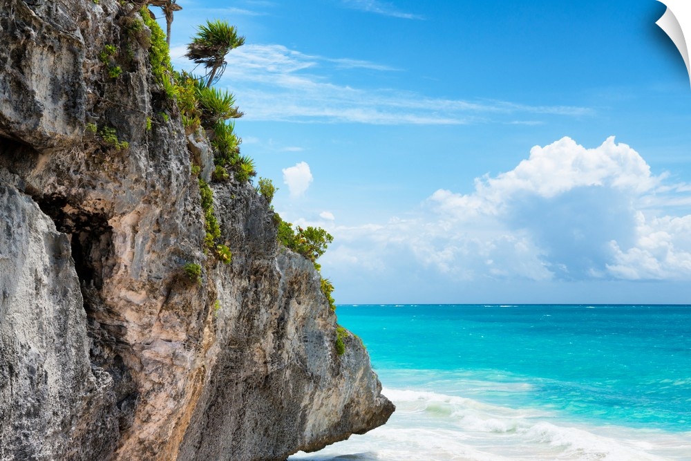 Photograph of a giant rock with tropical vegetation and palm trees hanging over the clear Caribbean ocean on a beautiful d...