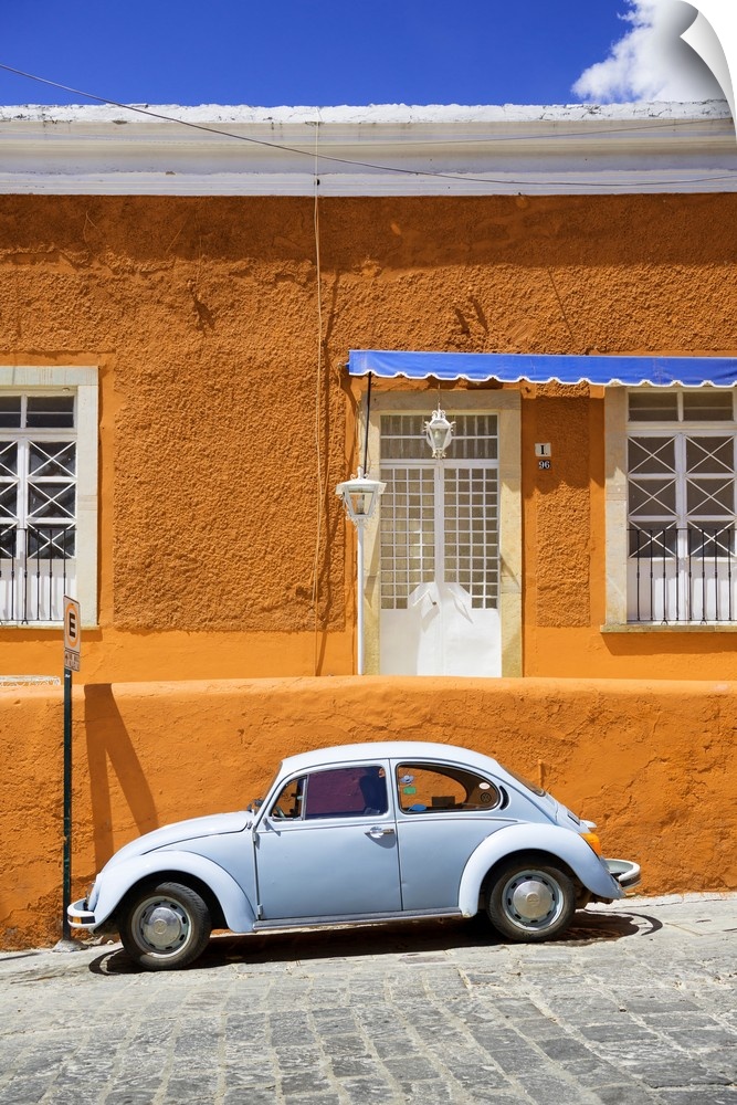 Photograph of a classic Volkswagen Beetle in front of an orange and blue building. From the Viva Mexico Collection.