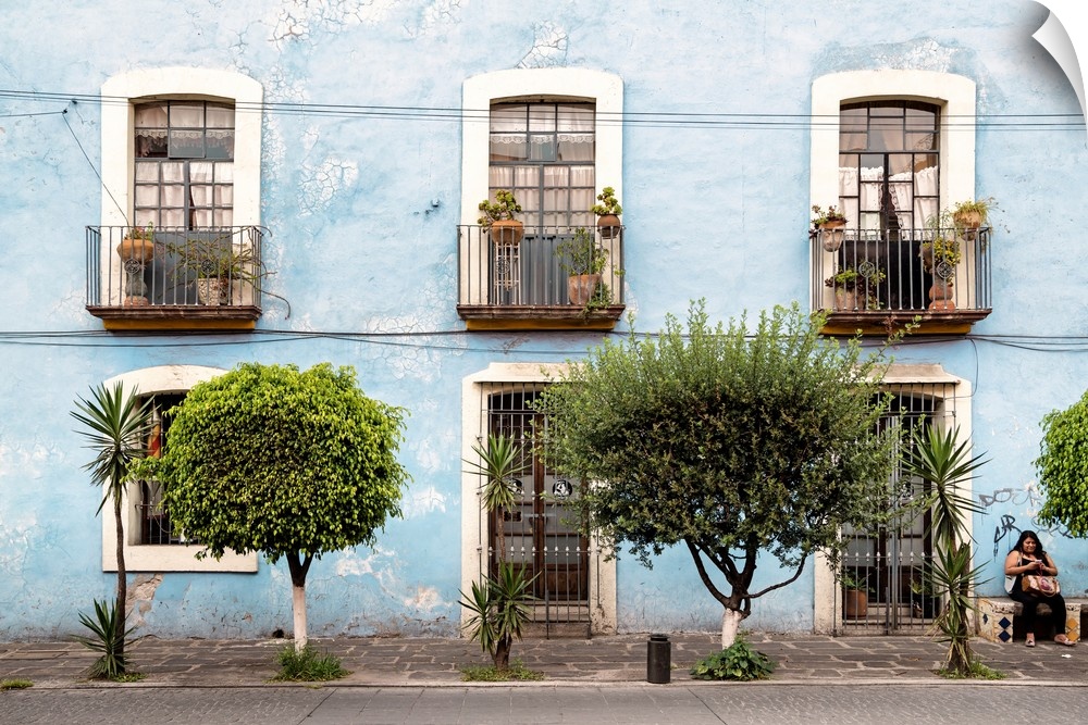 Photograph of a light blue exterior lined with windows, doors, and trees. From the Viva Mexico Collection.