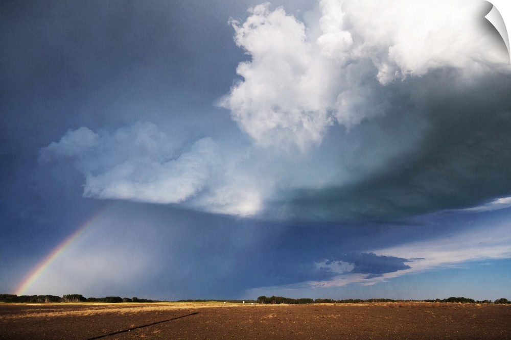 Photograph of a prairie landscape with a rainbow formed underneath dark clouds.