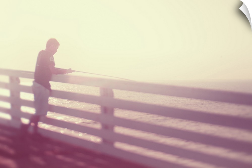 Pictorialist photo of a person fishing from the pier in the sunshine in pink hues.