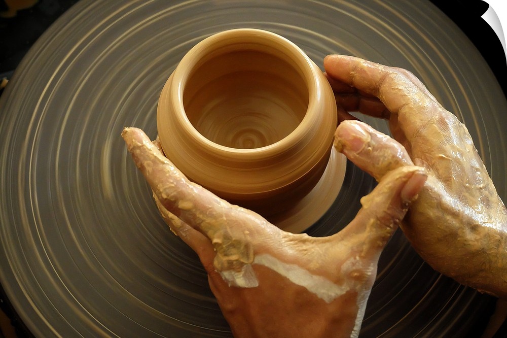 A potter shaping clay with their hands on a spinning pottery wheel.