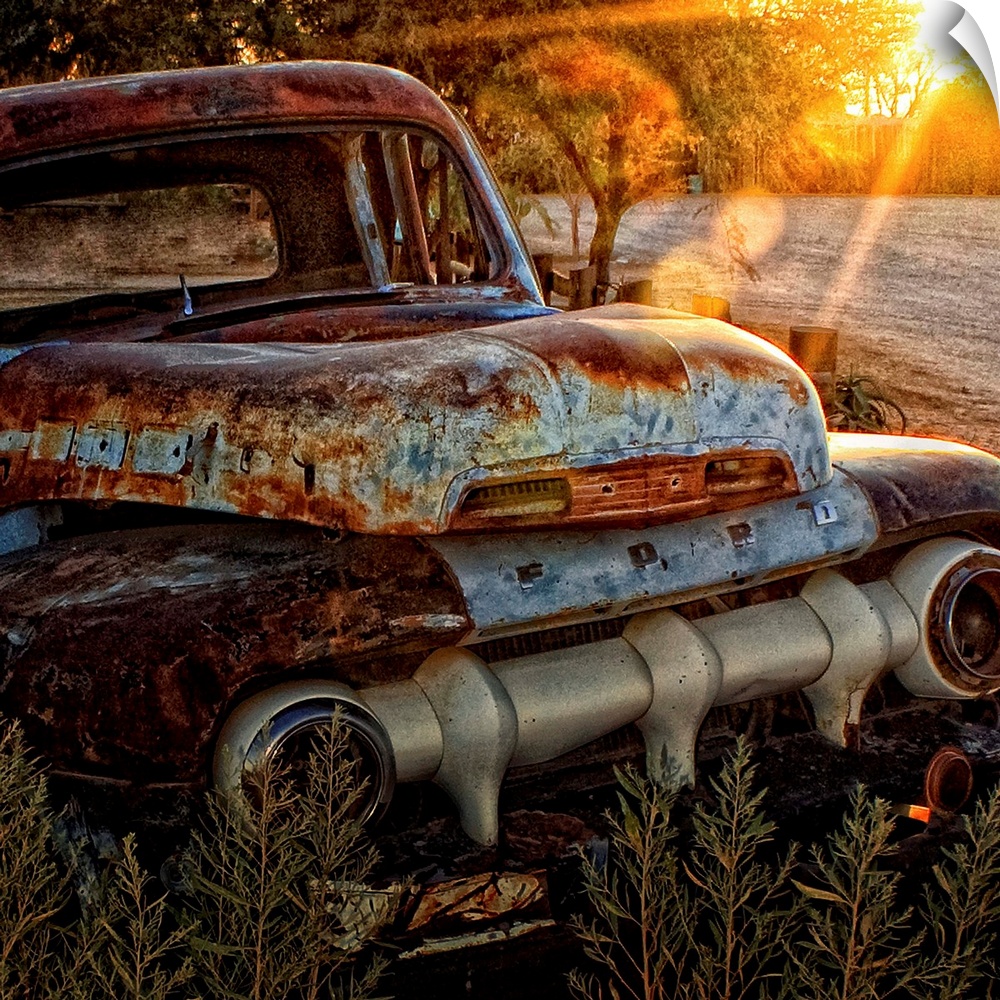 An old abandoned Ford car covered in rust in the sunset.