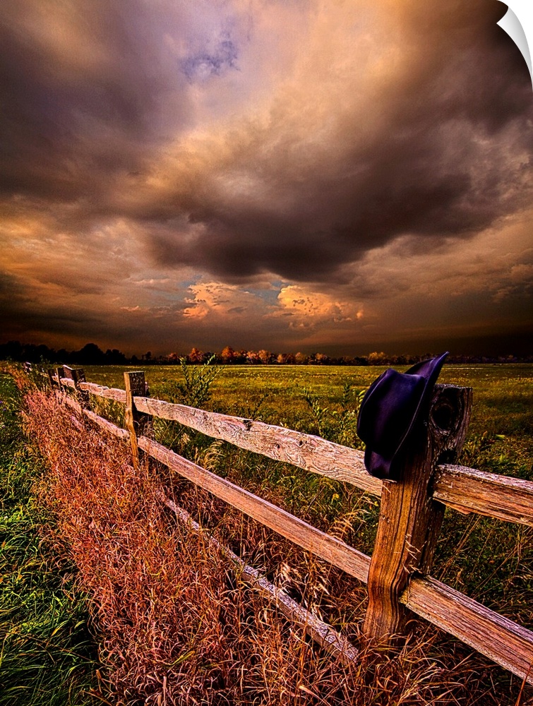 A hat resting on the post of a wooden fence under a cloudy sky.