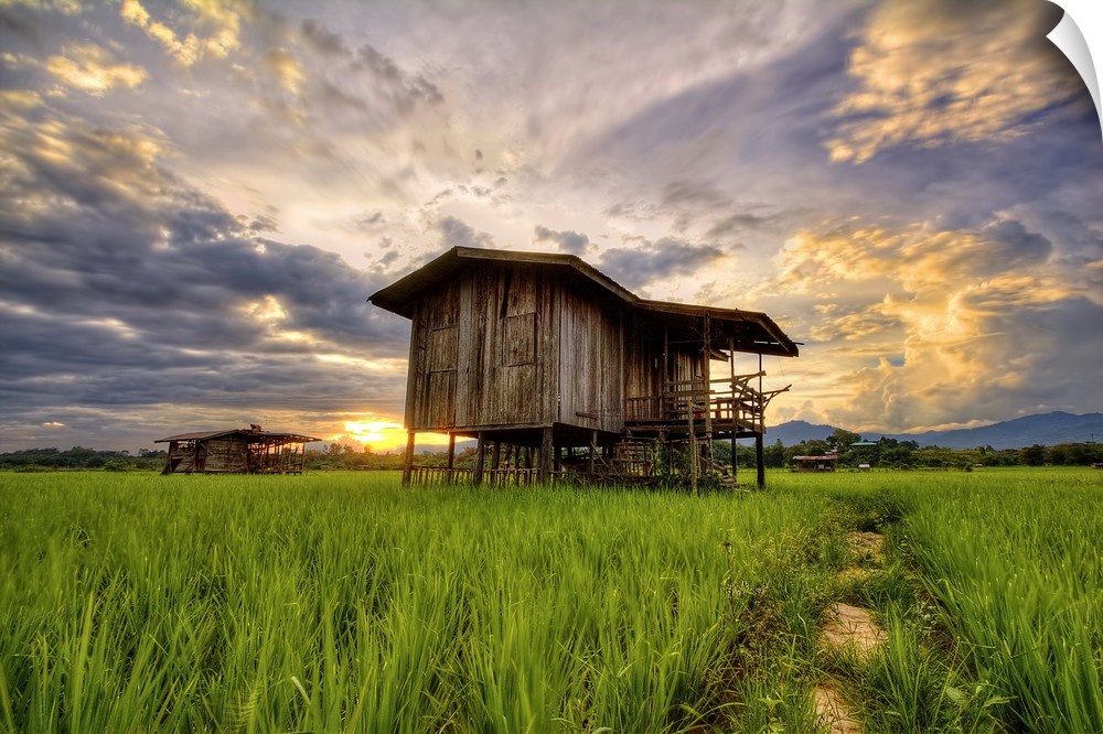 An old wooden building in a field under a colorful sunset sky.