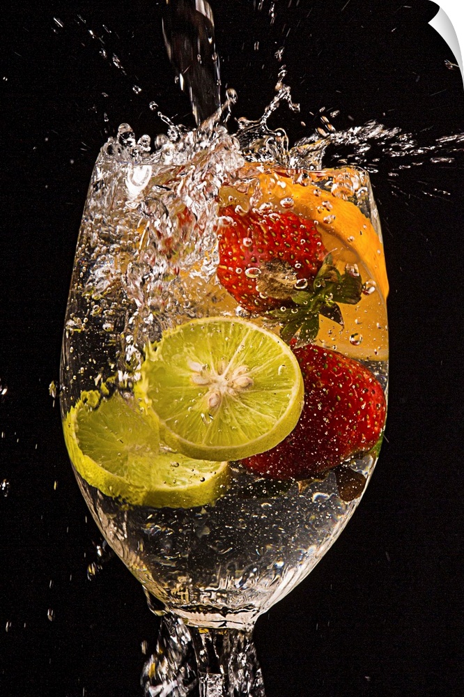 Slices of lemons and oranges and whole strawberries splashing into a glass of water.