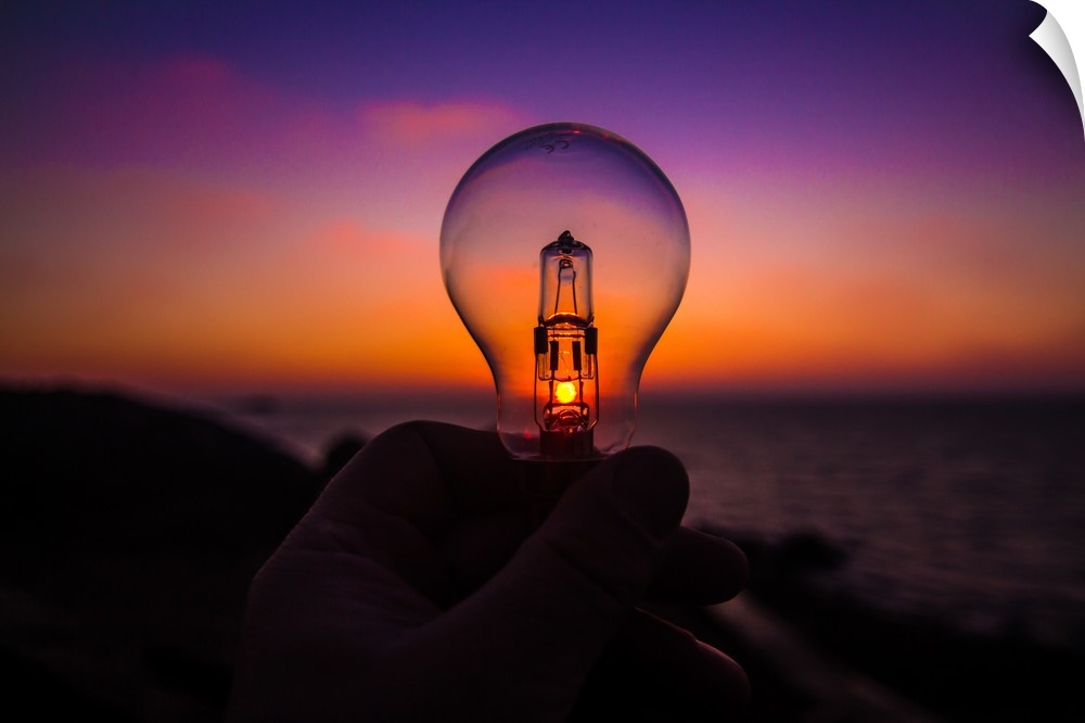 A lighbulb held against the sunset, appearing to shine with the light from the sun.