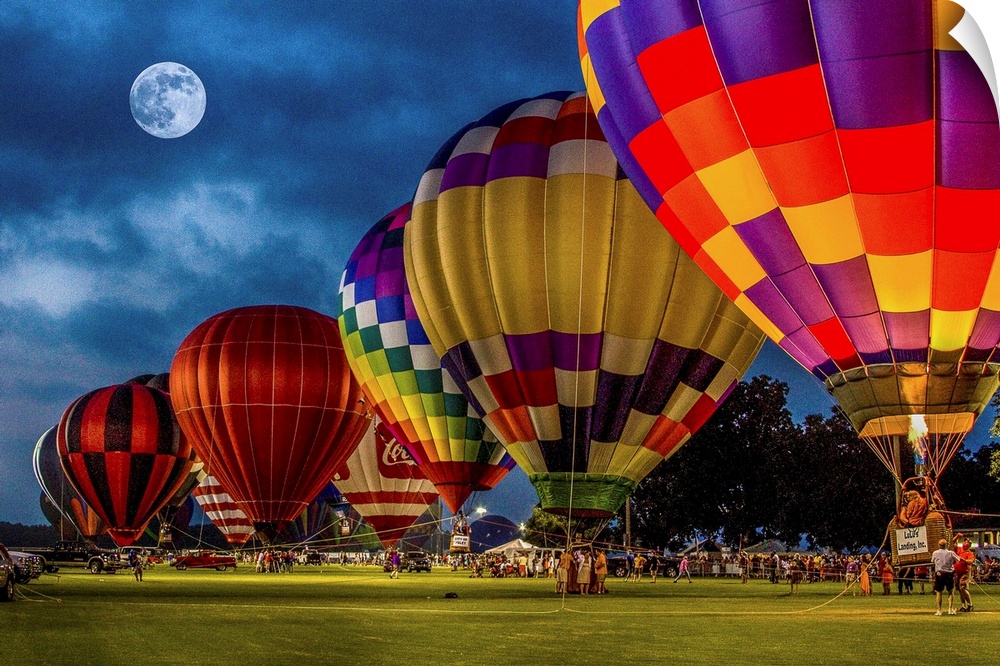 Moon in the night sky over a row of colorful hot air balloons.