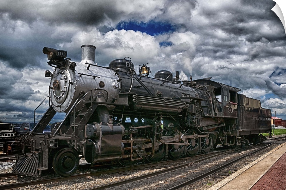 Photograph of an old steam engine sitting on train train under a dramatic cloudy sky.