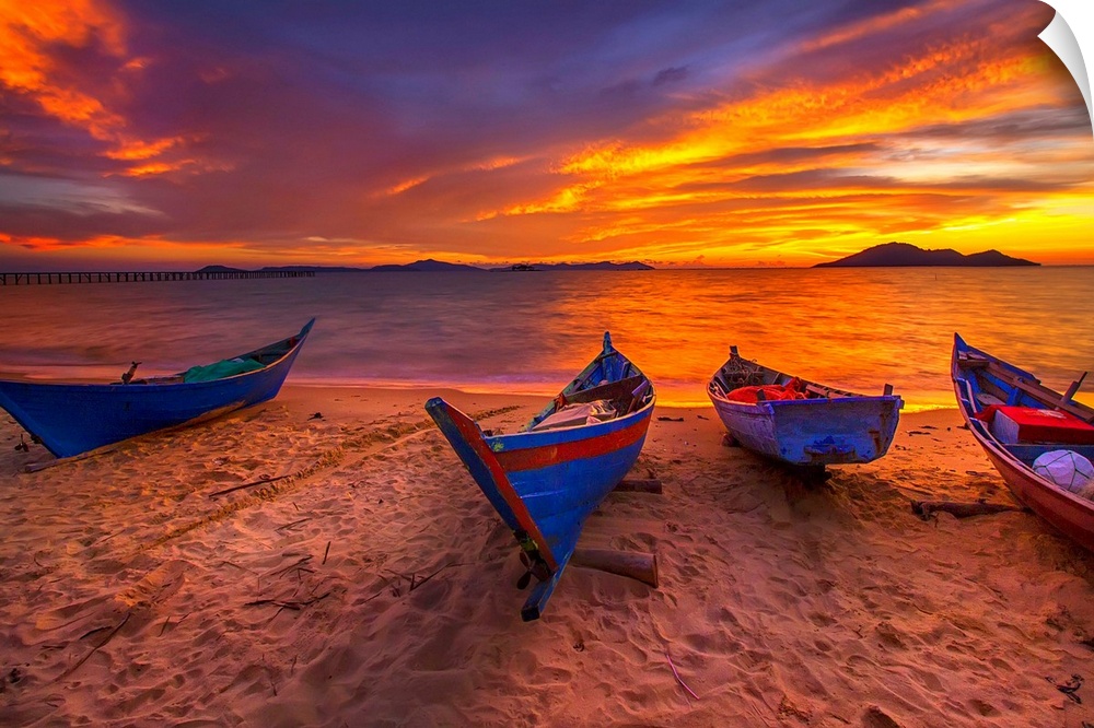 A row of small blue boats resting on the sandy beach with a brilliant sunrise.