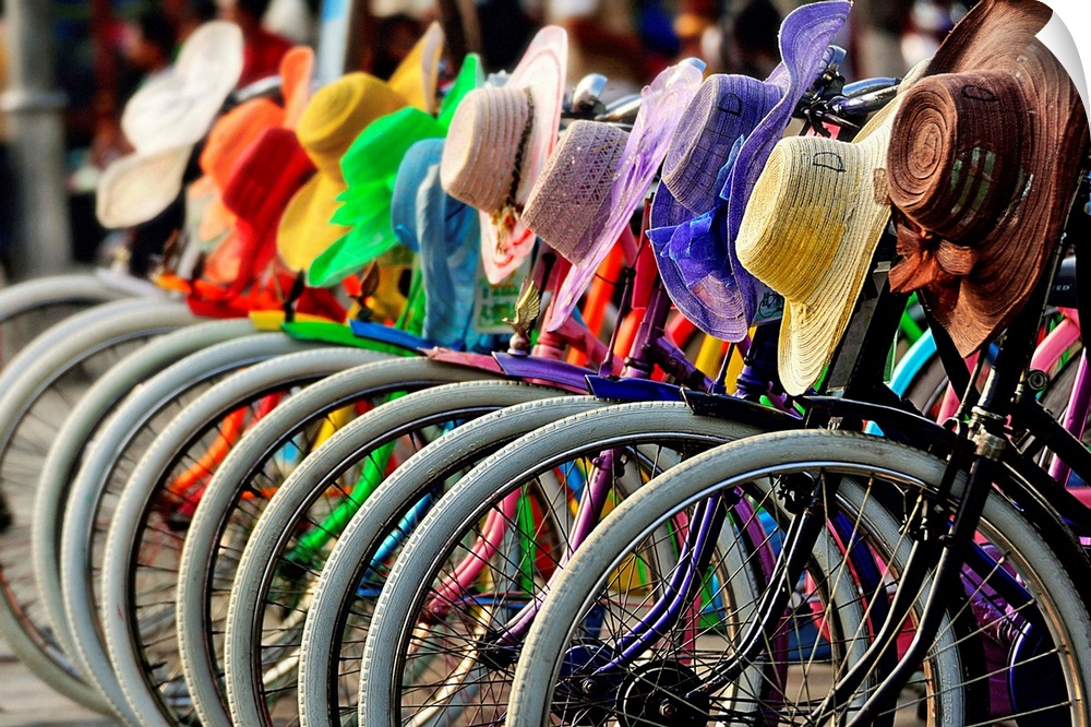 A row of bicycles with rainbow hats hanging on the handlebars.