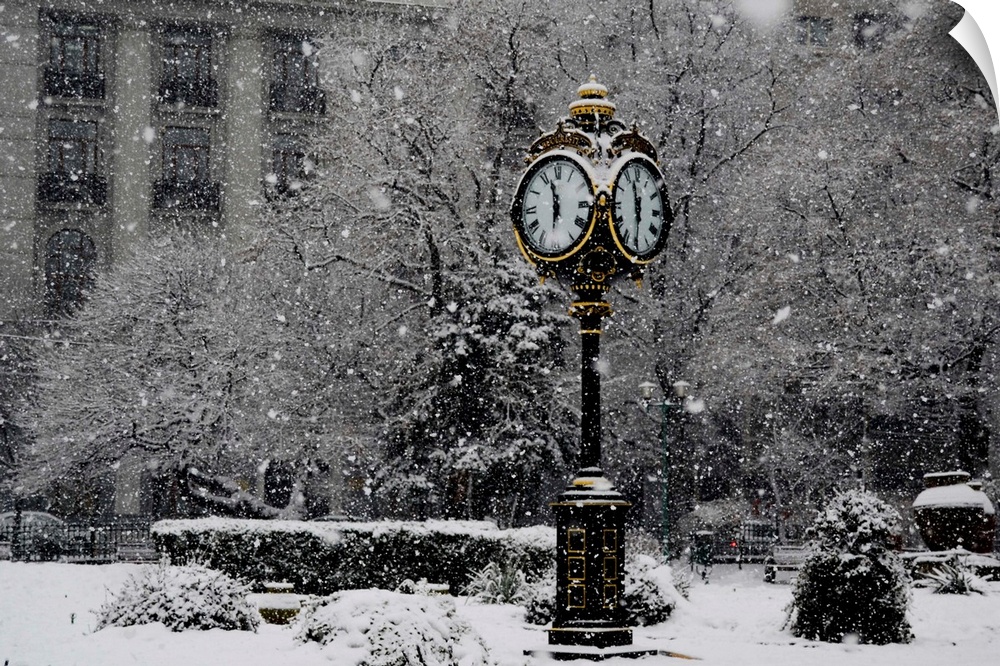 A large clock standing in a park while snow falls around it.