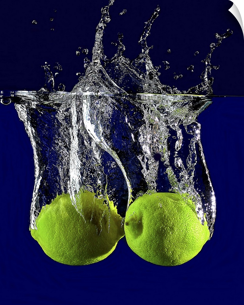 Two green limes dropped into clear water.