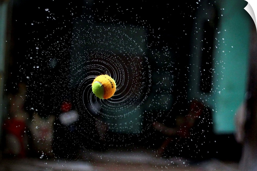 Dynamic photograph of a thrown tennis ball in a spinning motion with water spraying off it.