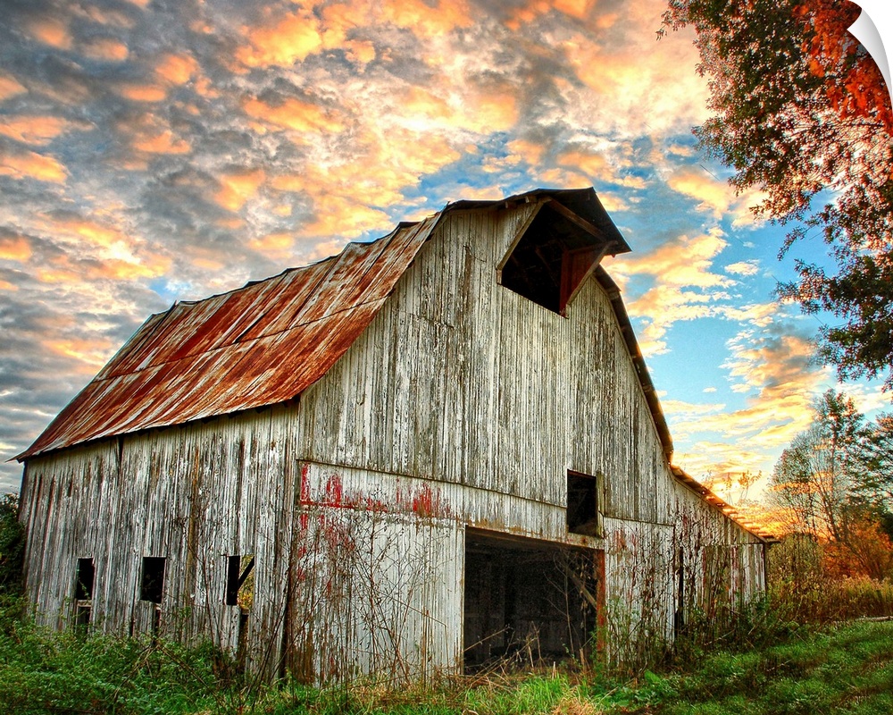 Sunset over an old, weathered barn, with a cloudy sky.
