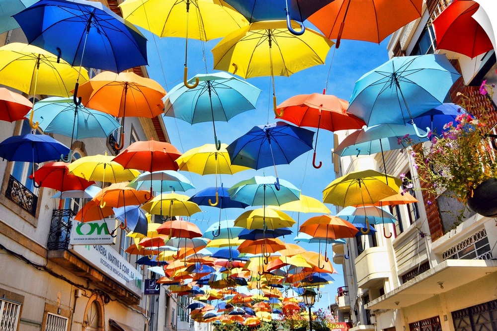 Colorful umbrellas hanging over a walkway in a village.