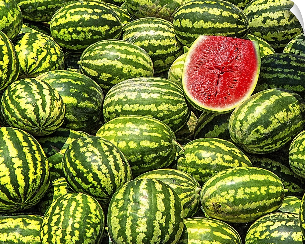 A big bunch of watermelons with one sliced in half, revealing the red fruit.
