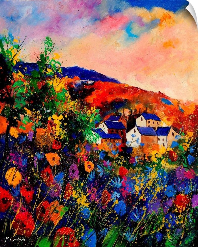 A field of multi-colored flowers in front of a group of houses on a colorful summer day in the countryside.
