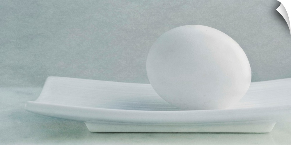 Simple, soft still life with a white chicken egg in a white dish