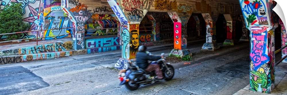 A person on a motorcycle drives past columns and sidewalks covered in colorful graffiti at the entrance of the Krog Street...