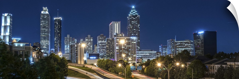 Panoramic photo of the city skyline of Atlanta, Georgia, illuminated at night against a deep blue sky, with light trails f...