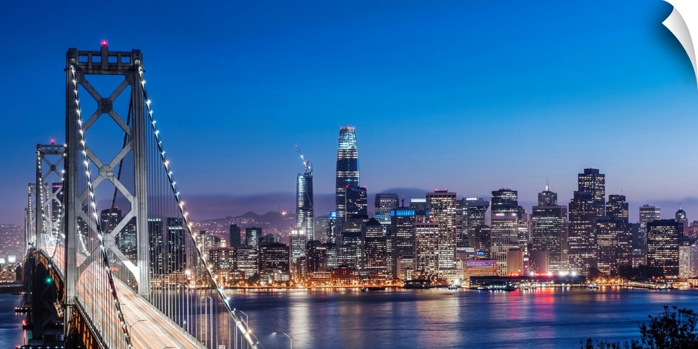 Photograph of the Bay Bridge and the San Francisco skyline lit up at dusk.