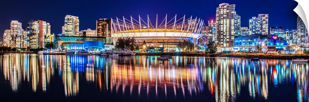 Panoramic photograph of BC Place Stadium and part of the Vancouver skyline lit up at night and reflecting onto the water, ...