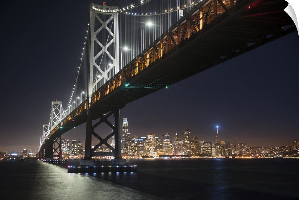 Photograph from below the Bay Bridge at night with the San Francisco skyline lit up in the background.